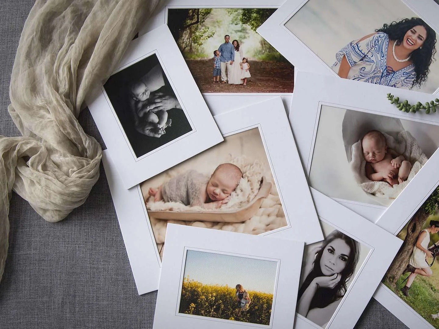A scattered pile of white-matted prints of families, babies and portraits