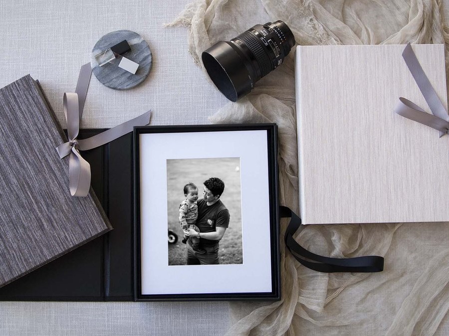 Two presentation boxes in grey linen with ribbon ties, beside a matted black and white print of a father and child